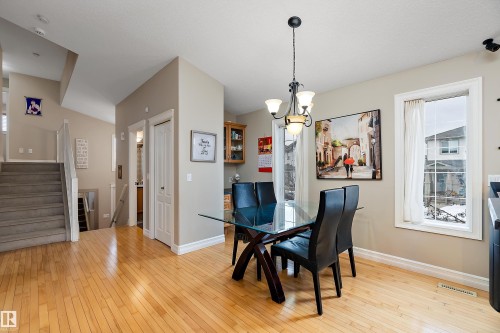 Bright dining area featuring hardwood-finish flooring, a contemporary chandelier, two windows with white trim, and a built-in cabinet with glass-front doors - 16748 118 Street Nw, Edmonton, AB - Indoor Photo Showing Dining Room