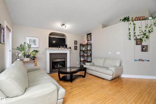 Living area featuring wood-finish flooring, a fireplace with a white mantel and tiled surround, and vaulted ceilings - 16748 118 Street Nw, Edmonton, AB - Indoor Photo Showing Living Room With Fireplace