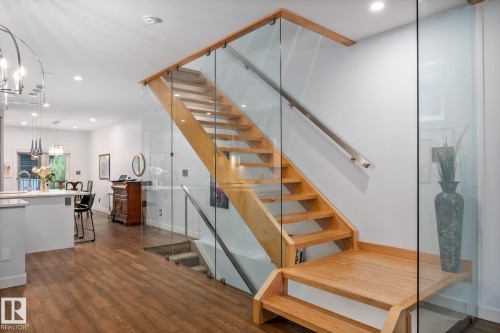 Contemporary open-tread staircase with wood-finish steps and glass panel railings, complemented by a stainless steel handrail - 14221 101 Avenue Nw, Edmonton, AB - Indoor Photo Showing Other Room