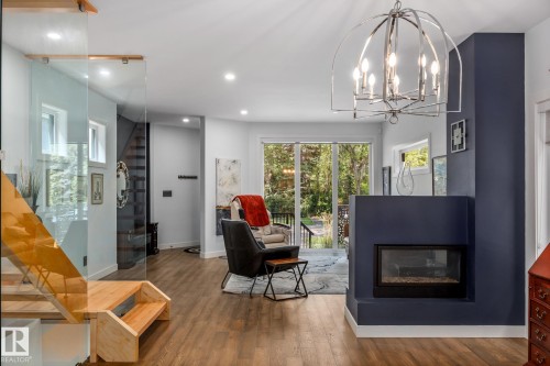 Living area featuring a modern fireplace with a dark accent wall, wood-finish flooring, recessed lighting, and a contemporary chandelier - 14221 101 Avenue Nw, Edmonton, AB - Indoor Photo Showing Living Room With Fireplace