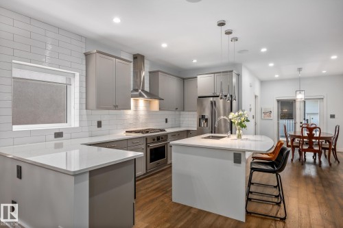 Open-concept kitchen featuring light gray cabinetry, white subway tile backsplash, stainless steel appliances, and wood-finish flooring - 14221 101 Avenue Nw, Edmonton, AB - Indoor Photo Showing Kitchen With Upgraded Kitchen