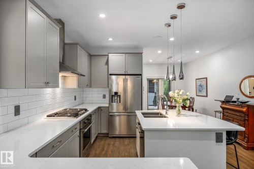 Modern kitchen featuring light gray cabinetry, stainless steel appliances, a white subway tile backsplash, and wood-finish flooring - 14221 101 Avenue Nw, Edmonton, AB - Indoor Photo Showing Kitchen With Double Sink With Upgraded Kitchen