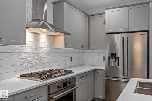 Modern kitchen featuring stainless steel appliances, including a gas range with an oven, a French door refrigerator with an ice and water dispenser, and a range hood - 14221 101 Avenue Nw, Edmonton, AB - Indoor Photo Showing Kitchen With Upgraded Kitchen