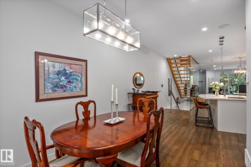 Dining area featuring a contemporary linear chandelier, wood-finish flooring, and light gray walls - 14221 101 Avenue Nw, Edmonton, AB - Indoor Photo Showing Dining Room
