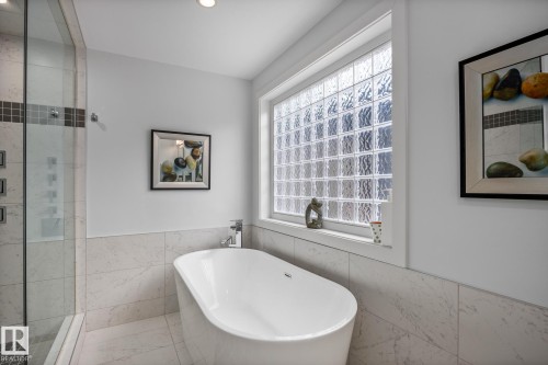 Freestanding bathtub accompanied by a glass block privacy window and full-height tiled walls - 14221 101 Avenue Nw, Edmonton, AB - Indoor Photo Showing Bathroom