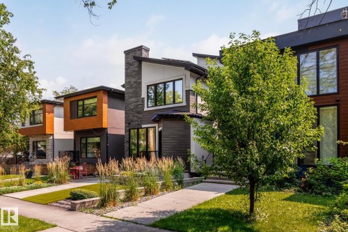 Contemporary exterior featuring multi-textured facades, expansive windows, a stone chimney, a flat roofline, and a concrete pathway with integrated landscaping - 14221 101 Avenue Nw, Edmonton, AB - Outdoor