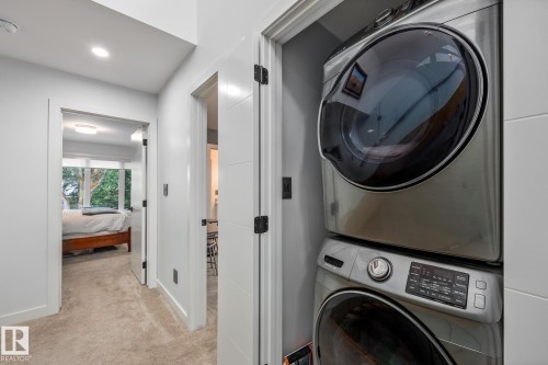 Integrated stacked washer and dryer in a dedicated closet, featuring modern controls and a sleek silver finish - 14221 101 Avenue Nw, Edmonton, AB - Indoor Photo Showing Laundry Room