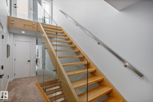 Modern staircase featuring light wood treads and risers, glass panel railings with brushed metal standoffs, and a brushed metal wall-mounted handrail - 14221 101 Avenue Nw, Edmonton, AB - Indoor Photo Showing Other Room