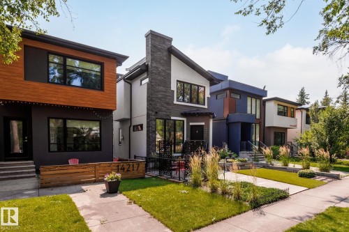 Contemporary exterior featuring a stone-clad chimney, dark framed windows, wood-finish siding, and a low-maintenance artificial turf front yard - 14221 101 Avenue Nw, Edmonton, AB - Outdoor With Facade