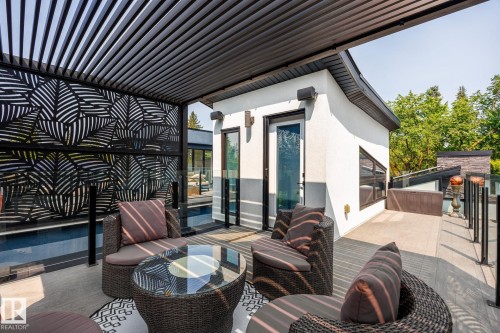 Rooftop deck featuring a louvered pergola, decorative privacy screen, glass railings, and a stucco exterior structure - 14221 101 Avenue Nw, Edmonton, AB - Outdoor With Deck Patio Veranda