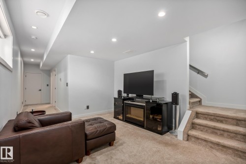 Finished lower level featuring recessed lighting, a built-in electric fireplace, light gray wall tones, and carpeted stairs with a modern handrail - 14221 101 Avenue Nw, Edmonton, AB - Indoor