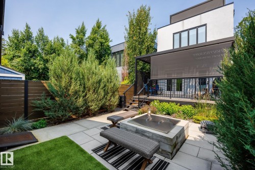 Landscaped backyard featuring a concrete paver patio, artificial turf area, built-in fire pit, and a dark wood privacy fence - 14221 101 Avenue Nw, Edmonton, AB - Outdoor With Deck Patio Veranda