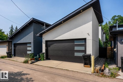 Contemporary garage exterior featuring a dark horizontal panel door with frosted glass inserts, light stucco finish, and a sloped black roofline - 14221 101 Avenue Nw, Edmonton, AB - Outdoor With Exterior