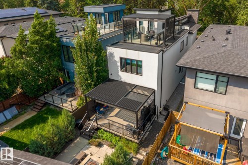 Modern white exterior featuring a rooftop deck with glass railings, a ground-level covered patio, and mature trees - 14221 101 Avenue Nw, Edmonton, AB - Outdoor With Deck Patio Veranda With Exterior