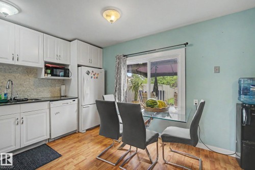 Kitchen featuring white cabinetry, dark countertops, a tiled backsplash, wood-finish flooring, and a large window - 18407 95A Avenue Nw, Edmonton, AB - Indoor