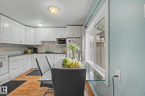 Kitchen featuring white cabinetry, dark countertops, a tiled backsplash, wood-finish flooring, and a large window - 18407 95A Avenue Nw, Edmonton, AB - Indoor