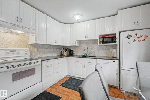 Kitchen featuring white cabinetry, dark countertops, a mosaic tile backsplash, and wood-finish flooring - 18407 95A Avenue Nw, Edmonton, AB - Indoor Photo Showing Kitchen