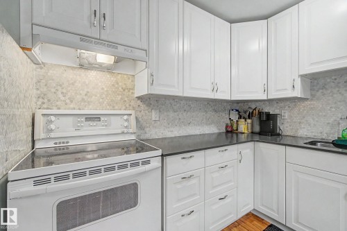 Kitchen featuring white shaker-style cabinetry, dark countertops, and a full tile backsplash - 18407 95A Avenue Nw, Edmonton, AB - Indoor Photo Showing Kitchen