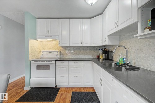 Kitchen featuring extensive white cabinetry, dark countertops, a tile backsplash, and wood-finish flooring - 18407 95A Avenue Nw, Edmonton, AB - Indoor Photo Showing Kitchen With Double Sink