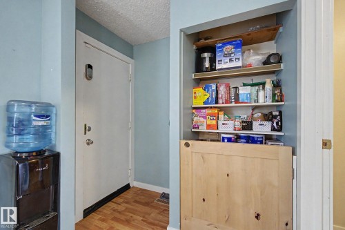 Entryway featuring wood-finish flooring, a white entry door with a digital lock, and a built-in closet with multiple shelving units and a light-toned wood-panel door - 18407 95A Avenue Nw, Edmonton, AB - Indoor Photo Showing Other Room