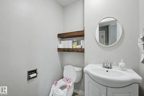 Bathroom featuring a white vanity with an integrated sink, a circular mirror, and two dark wood floating shelves - 18407 95A Avenue Nw, Edmonton, AB - Indoor Photo Showing Bathroom