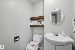 Bathroom featuring a white vanity with an integrated sink, a circular mirror, and two dark wood floating shelves - 