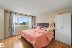 Bedroom featuring wood-finish flooring, a multi-pane window with a white frame, and a white built-in wardrobe with panel detailing and silver hardware - 