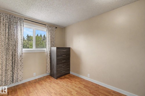 Window with white trim and view of mature trees, wood-finish flooring, light beige wall paint, white baseboards, and a textured ceiling - 18407 95A Avenue Nw, Edmonton, AB - Indoor