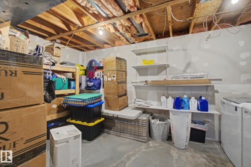 Unfinished basement space featuring exposed wooden ceiling joists, concrete flooring, built-in shelving units, and a visible washer appliance - 18407 95A Avenue Nw, Edmonton, AB - Indoor Photo Showing Basement