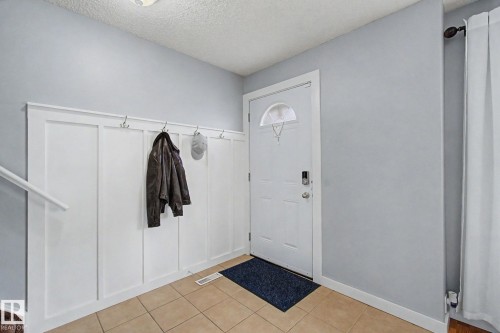 Entryway featuring a white board and batten wall with integrated hooks, light-toned tile flooring, and a white entry door with an arched glass insert - 18407 95A Avenue Nw, Edmonton, AB - Indoor Photo Showing Other Room