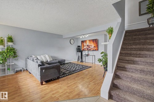 Living area featuring light wood-finish flooring, light grey wall paint, and a carpeted staircase with white trim - 18407 95A Avenue Nw, Edmonton, AB - Indoor