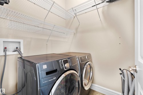 Dedicated laundry area featuring overhead wire shelving, a wall-mounted utility box, and tile flooring - 1338 Rutherford Road Sw, Edmonton, AB - Indoor Photo Showing Laundry Room
