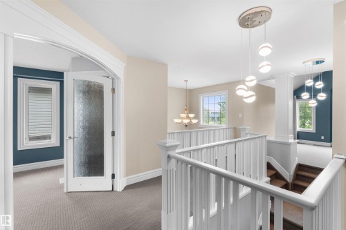Upper-level landing featuring a white spindle railing system, light neutral wall paint, and multiple pendant light fixtures - 1338 Rutherford Road Sw, Edmonton, AB - Indoor Photo Showing Other Room