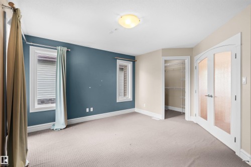 Carpeted room featuring a ceiling-mounted light fixture, two windows with blinds, a closet with wire shelving, and a double-door entry with frosted glass panels - 1338 Rutherford Road Sw, Edmonton, AB - Indoor