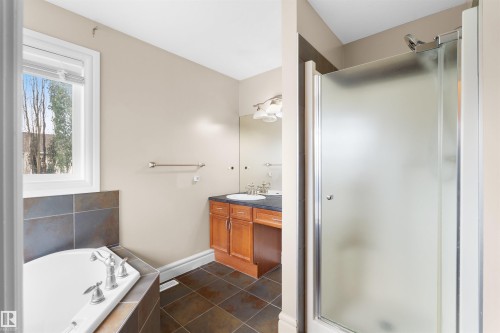 Bathroom featuring a corner soaking tub with tiled surround, a separate shower with frosted glass enclosure, a single vanity with wood cabinetry, and tiled flooring - 1338 Rutherford Road Sw, Edmonton, AB - Indoor Photo Showing Bathroom