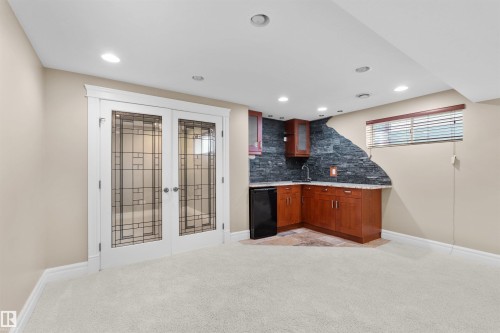 Finished lower level featuring a wet bar with stone backsplash, wood cabinetry, and a compact refrigerator - 1338 Rutherford Road Sw, Edmonton, AB - Indoor