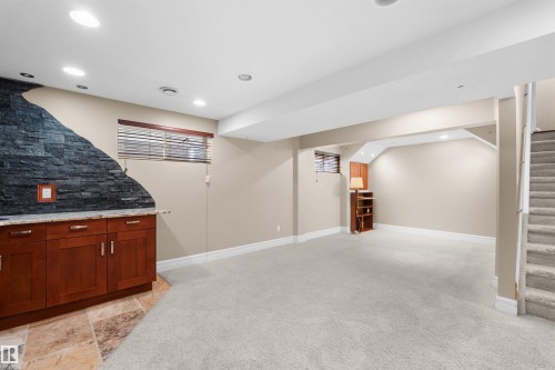 Spacious lower-level area featuring recessed lighting, a built-in wet bar with wood cabinetry and a stone-finish countertop, a stone accent wall, and neutral carpeting - 1338 Rutherford Road Sw, Edmonton, AB - Indoor Photo Showing Basement