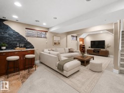 Finished lower level featuring recessed lighting, a built-in wet bar with stone-look countertop and wood cabinetry, and a stone accent wall - 