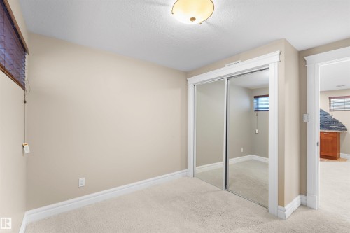 Carpeted room featuring mirrored sliding closet doors, white trim, a flush-mount ceiling light, and a window with blinds - 1338 Rutherford Road Sw, Edmonton, AB - Indoor Photo Showing Other Room
