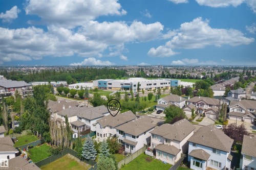 Aerial perspective showcasing a residential neighborhood with detached homes, mature trees, and a distant institutional building with a blue facade - 1338 Rutherford Road Sw, Edmonton, AB - Outdoor With View