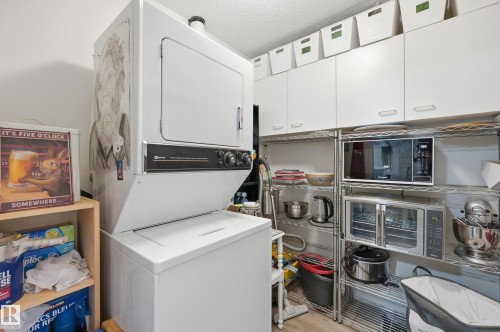 Stackable washer and dryer unit, complemented by extensive white cabinetry and wire shelving for organized storage - #208 9760 176 St Nw, Edmonton, AB - Indoor Photo Showing Laundry Room