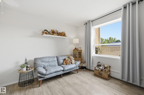 Bright room featuring wood-finish flooring and a large window with light-colored drapes - #208 9760 176 St Nw, Edmonton, AB - Indoor Photo Showing Living Room