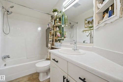 Full bathroom featuring a white tub/shower combination with a dual-head shower fixture, a white toilet, and wood-finish flooring - #208 9760 176 St Nw, Edmonton, AB - Indoor Photo Showing Bathroom