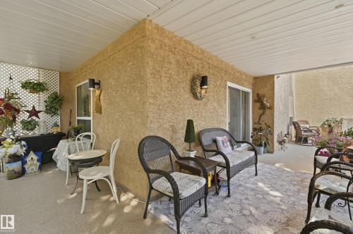 Covered patio featuring a stucco exterior, white lattice wall, two ceiling-mounted light fixtures, and a sliding glass door - #208 9760 176 St Nw, Edmonton, AB - Outdoor With Deck Patio Veranda With Exterior