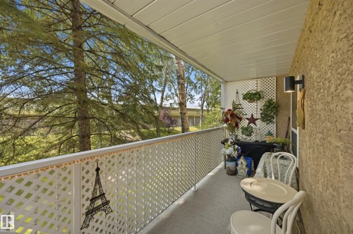 Covered balcony featuring a textured exterior wall, white lattice railing, and a slatted ceiling - #208 9760 176 St Nw, Edmonton, AB - Outdoor With Exterior