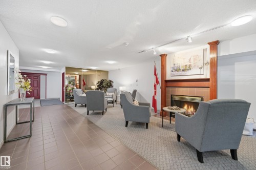 Welcoming common area featuring a fireplace with a wood mantle and tile surround, recessed lighting, track lighting, and a combination of tile and carpet flooring - #208 9760 176 St Nw, Edmonton, AB - Indoor With Fireplace