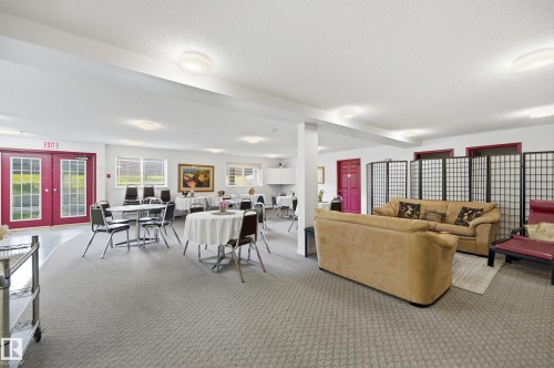 Spacious common area featuring textured carpet, multiple windows, a set of double glass-paneled doors, and recessed lighting - #208 9760 176 St Nw, Edmonton, AB - Indoor
