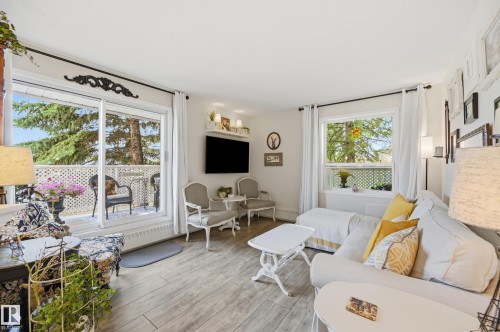 Living area featuring wood-finish flooring, a large sliding glass door opening to a private balcony, and a window with natural light - #208 9760 176 St Nw, Edmonton, AB - Indoor Photo Showing Living Room