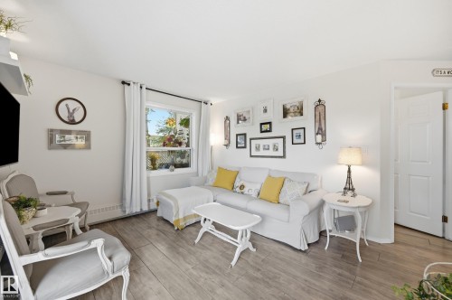 Bright living space featuring wood-finish flooring, white walls, and a large window with white curtain panels - #208 9760 176 St Nw, Edmonton, AB - Indoor Photo Showing Living Room
