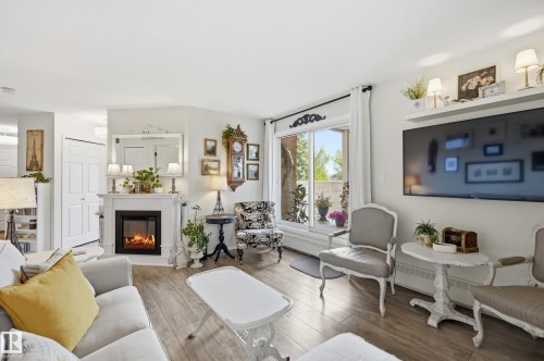 Open concept living area featuring wood-finish flooring, a white mantel fireplace, and a large sliding glass door - #208 9760 176 St Nw, Edmonton, AB - Indoor Photo Showing Living Room With Fireplace